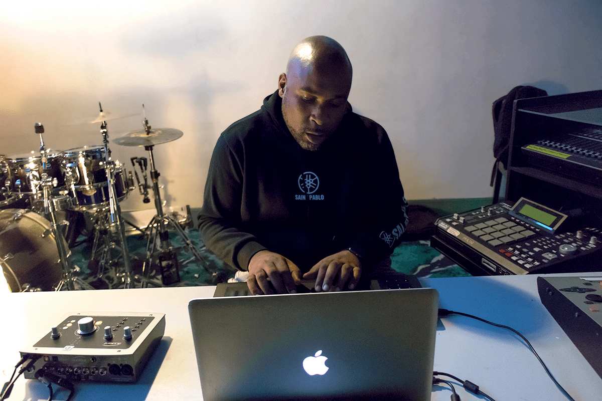 Chris Brown working at the desk beside a drum kit and sampler